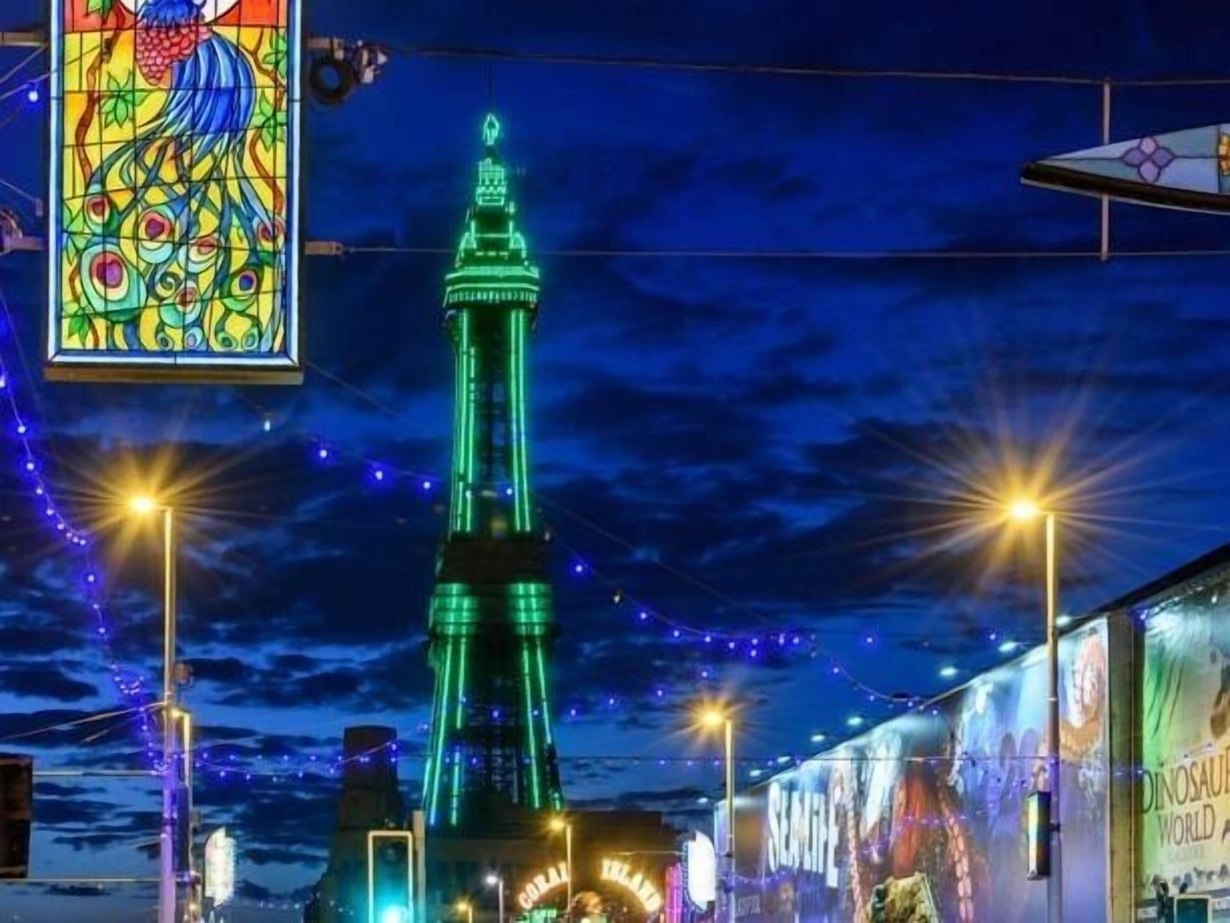 A nighttime view of a tall tower with green lighting, surrounded by string lights and a stained glass window.