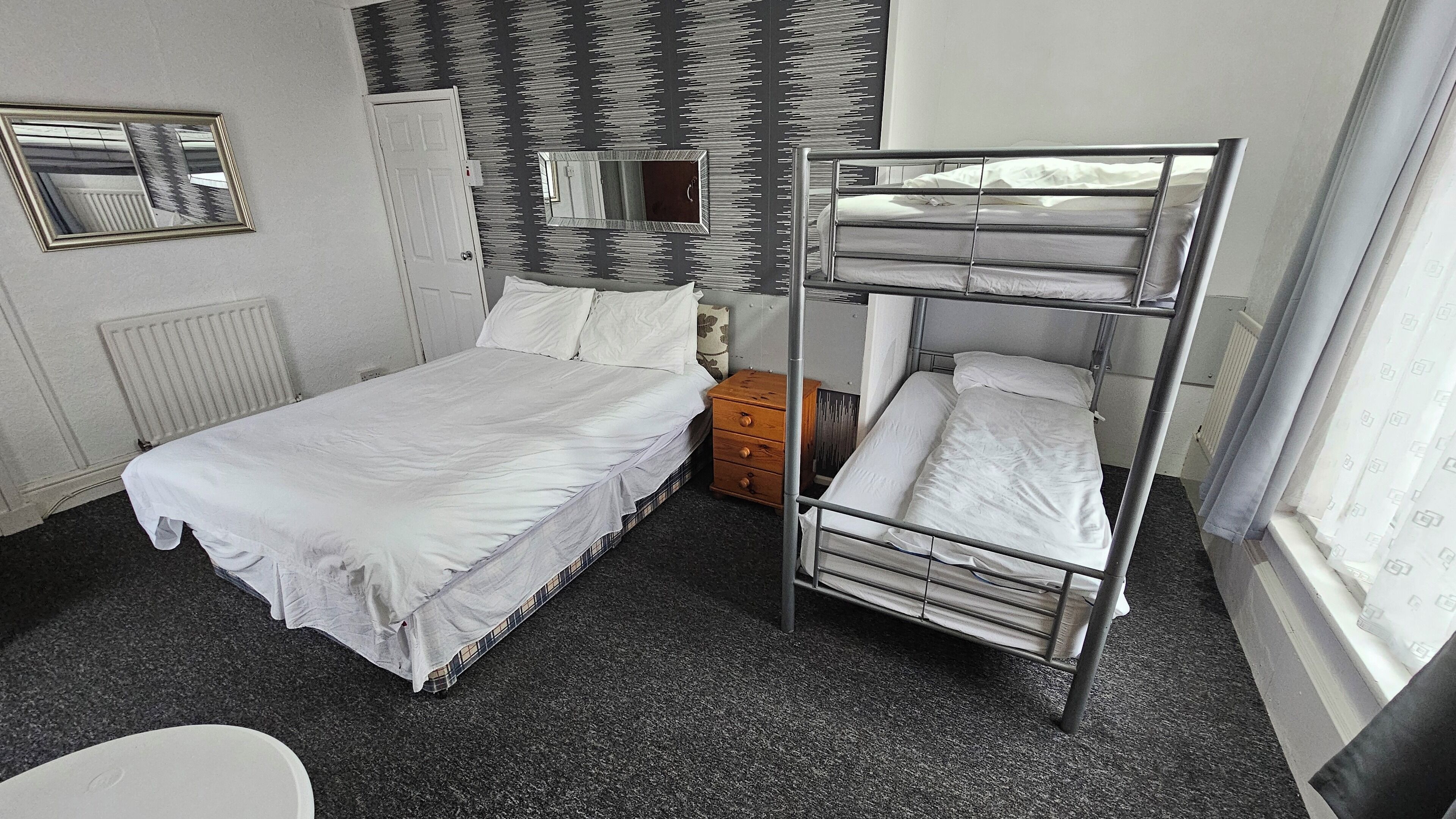 Une chambre d’hôtel avec un lit superposé, un lit simple, une table de chevet, un miroir et un radiateur.