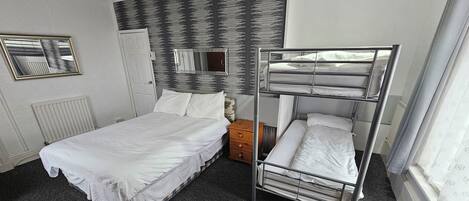 Une chambre d’hôtel avec un lit superposé, un lit simple, une table de chevet, un miroir et un radiateur.