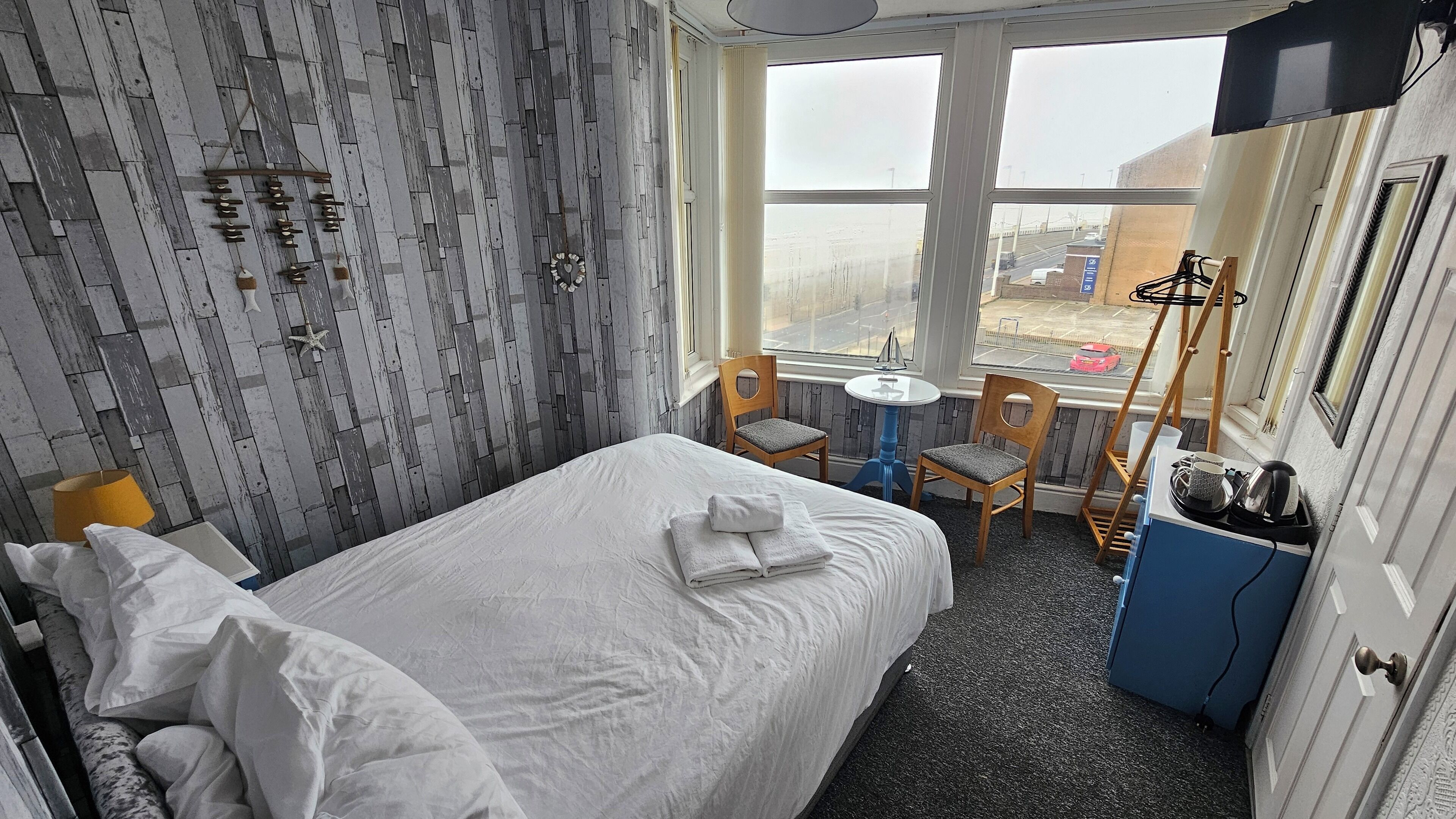 A hotel room with a bed, a small table, two chairs, a TV, and a view of the outside.
