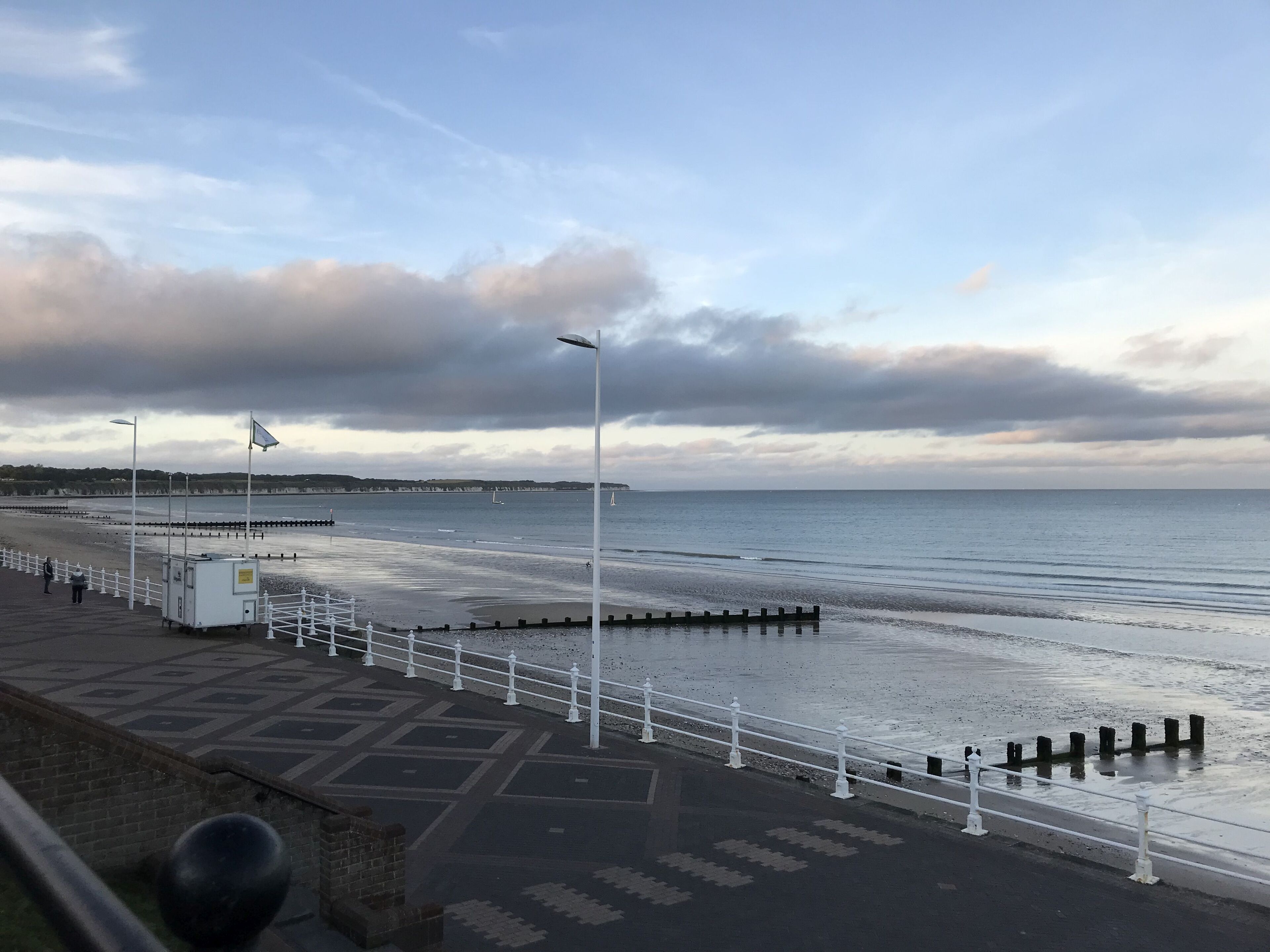 Un paseo marítimo costero con vista al mar, una cerca blanca y un camino pavimentado.