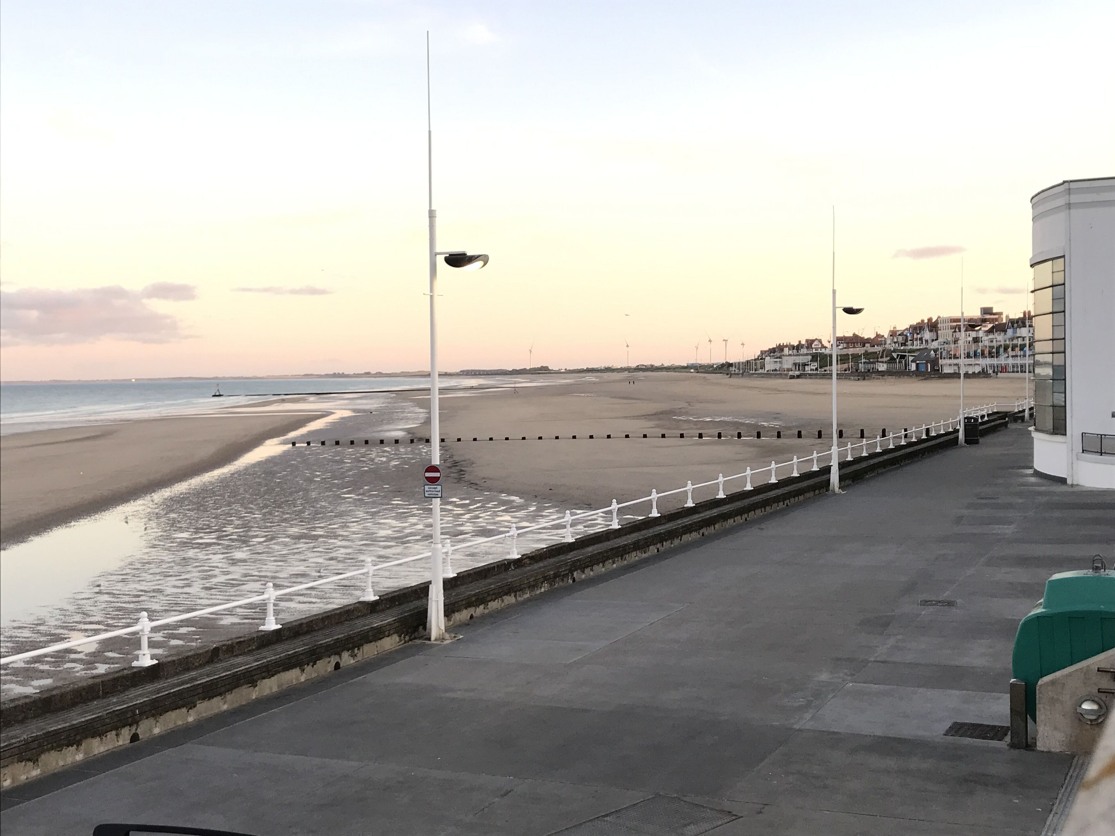 Une promenade en bord de mer avec une rambarde blanche, un panneau indiquant l’interdiction d’accès, et une vue sur la plage et l’océan.