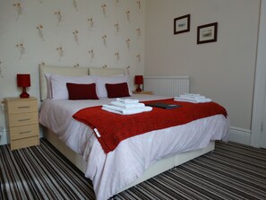 A neatly made bed with white and red bedding, two bedside tables with lamps, and a striped carpet.