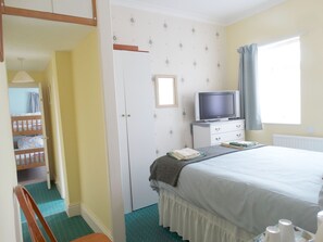 A bedroom with a bed, a television on a dresser, a window with curtains, and a door leading to a bathroom.