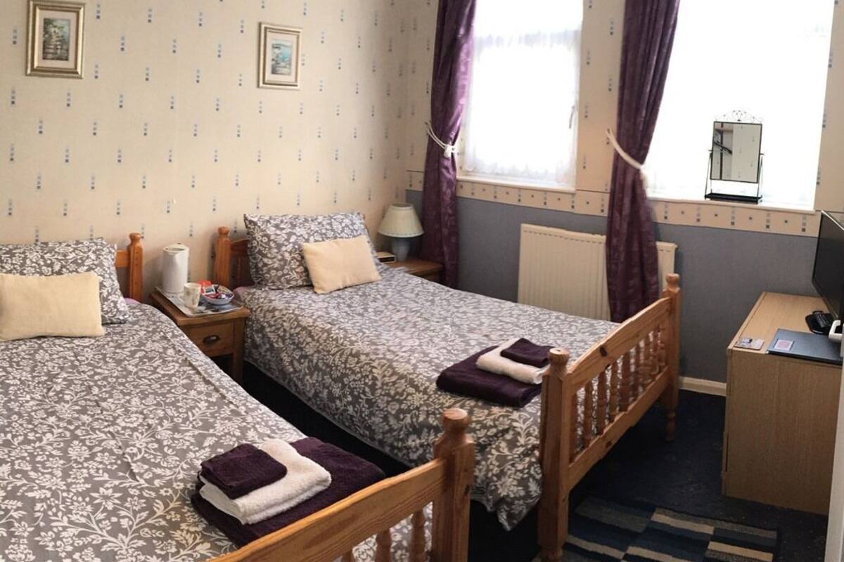 A room with two beds, a desk, and a window with curtains.