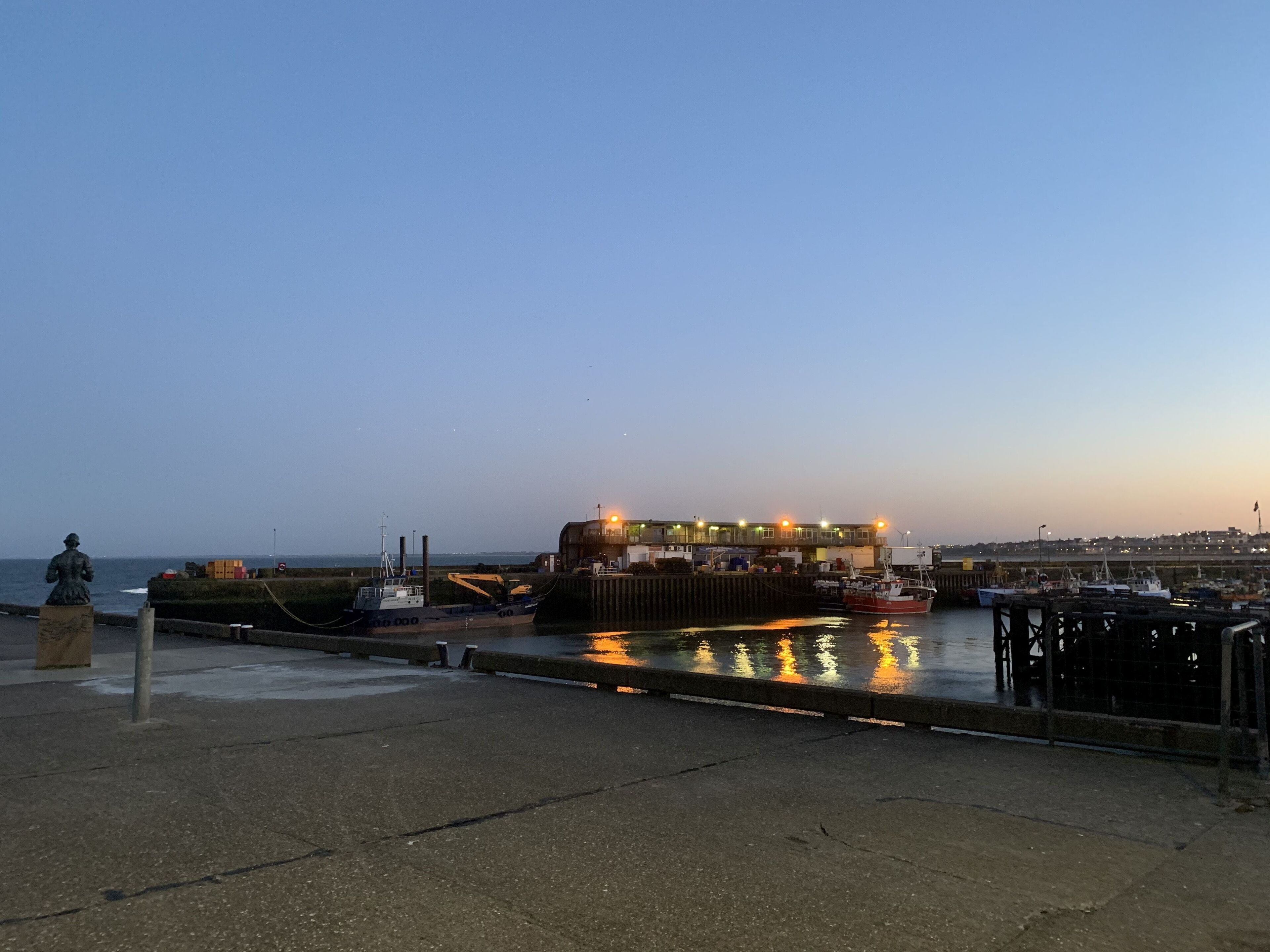 Une scène au bord de l’eau, avec un bateau amarré, une statue et un bâtiment illuminé.