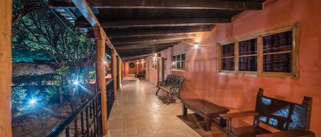 A corridor with wooden benches and a railing, leading to a room with a window and a bench.