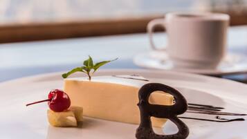 A dessert on a plate with a cherry and mint garnish, a chocolate letter 'B', and a cup in the background.