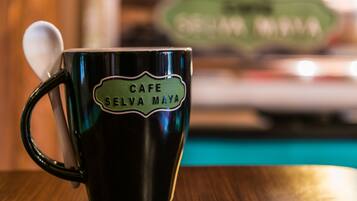 Una taza verde oscuro con una cuchara, con la etiqueta 'CAFE SELVA MAYA', sobre una mesa de madera.