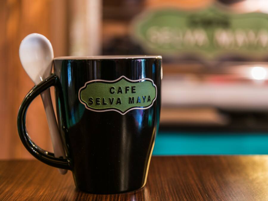 Una taza verde oscuro con una cuchara, con la etiqueta 'CAFE SELVA MAYA', sobre una mesa de madera.