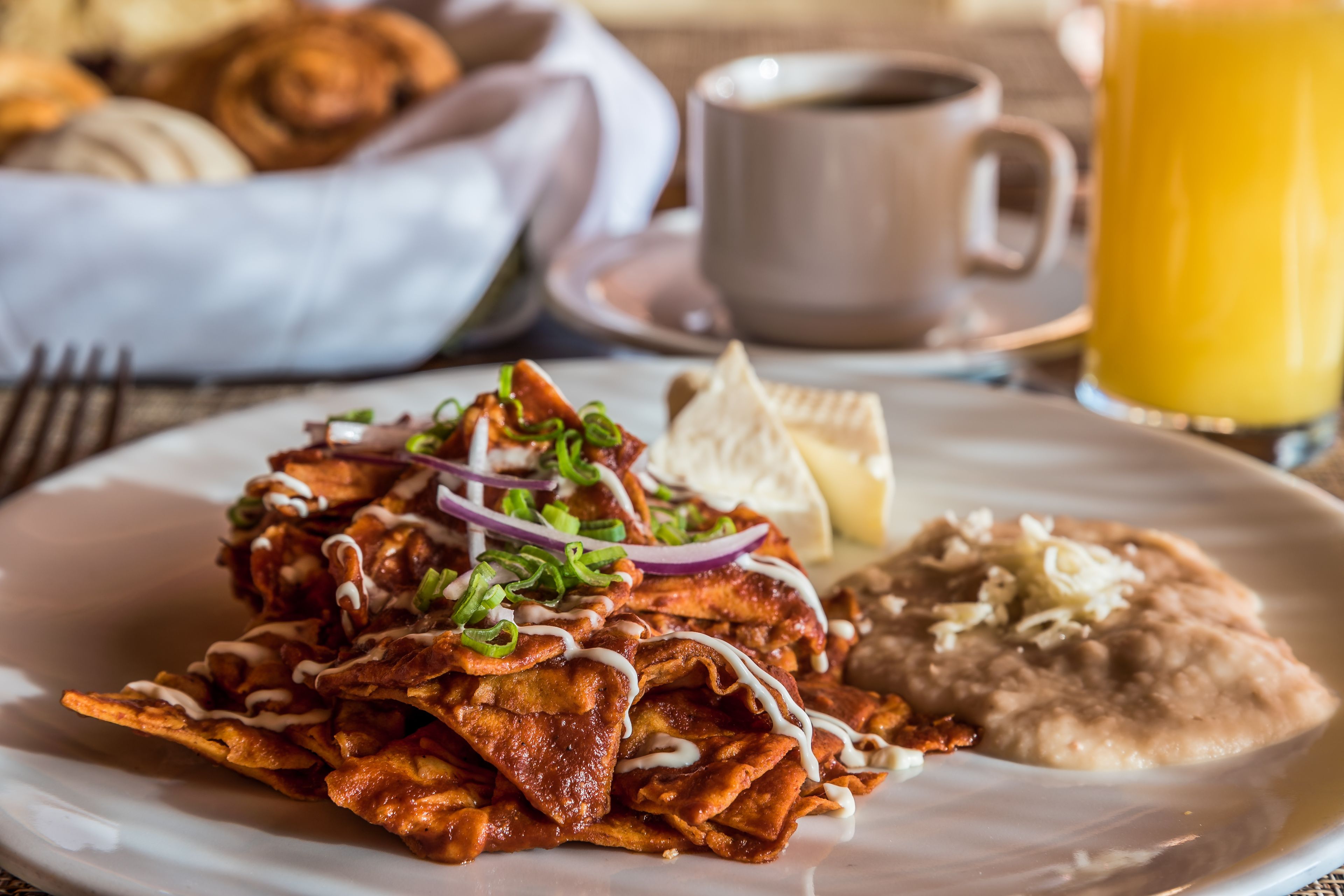 Un plato de nachos, una taza de café y un vaso de zumo de naranja sobre una mesa.
