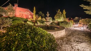 A hotel with a fountain and well-maintained gardens at night.