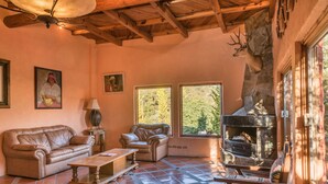 A cozy living room with a stone fireplace, leather sofas, and a large window overlooking greenery.