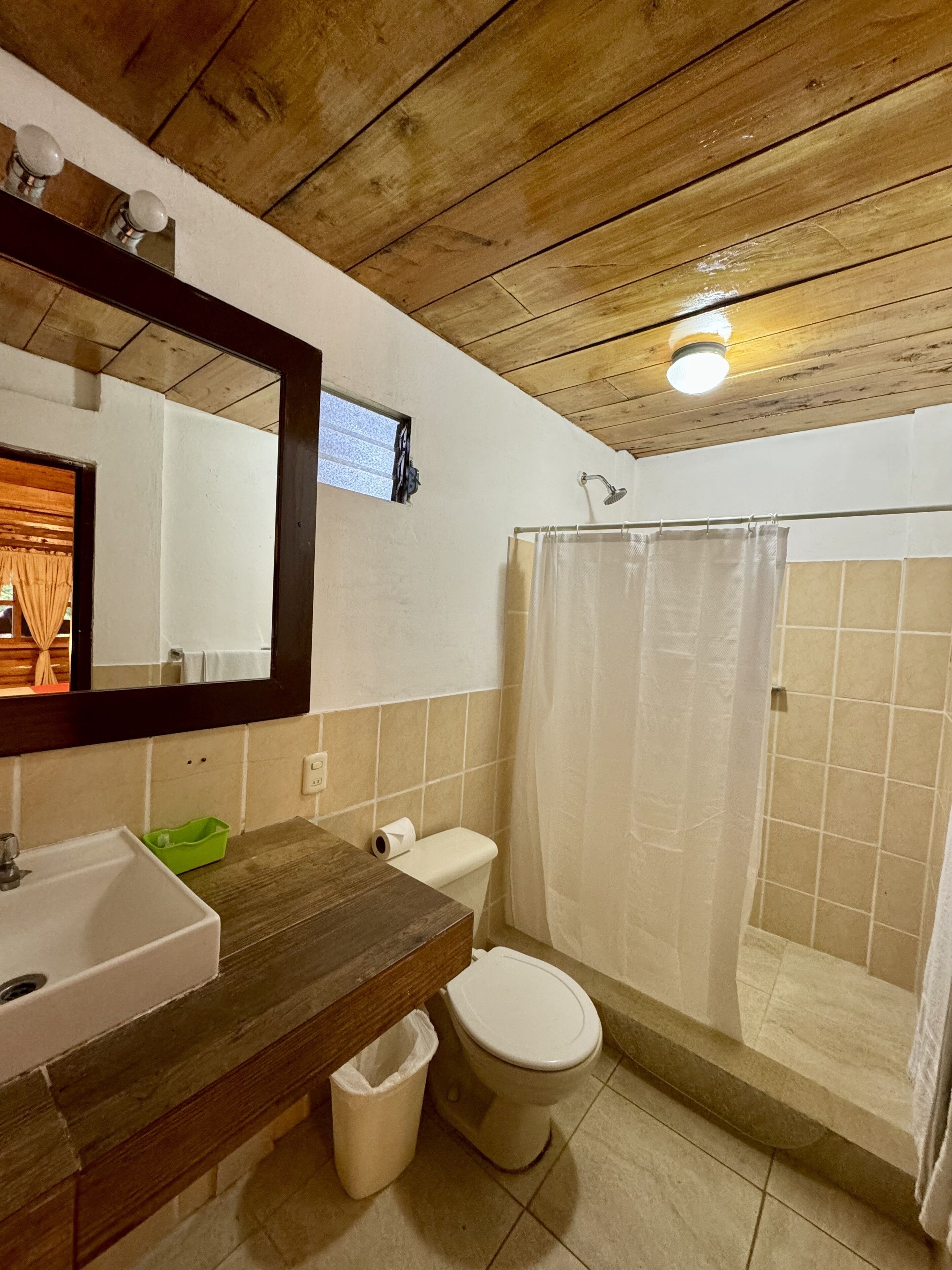 Ein Badezimmer mit einem Holzlagerflächen, einem Waschbecken, einer Toilette, einer Duschkabine mit Vorhang und einem Spiegel.