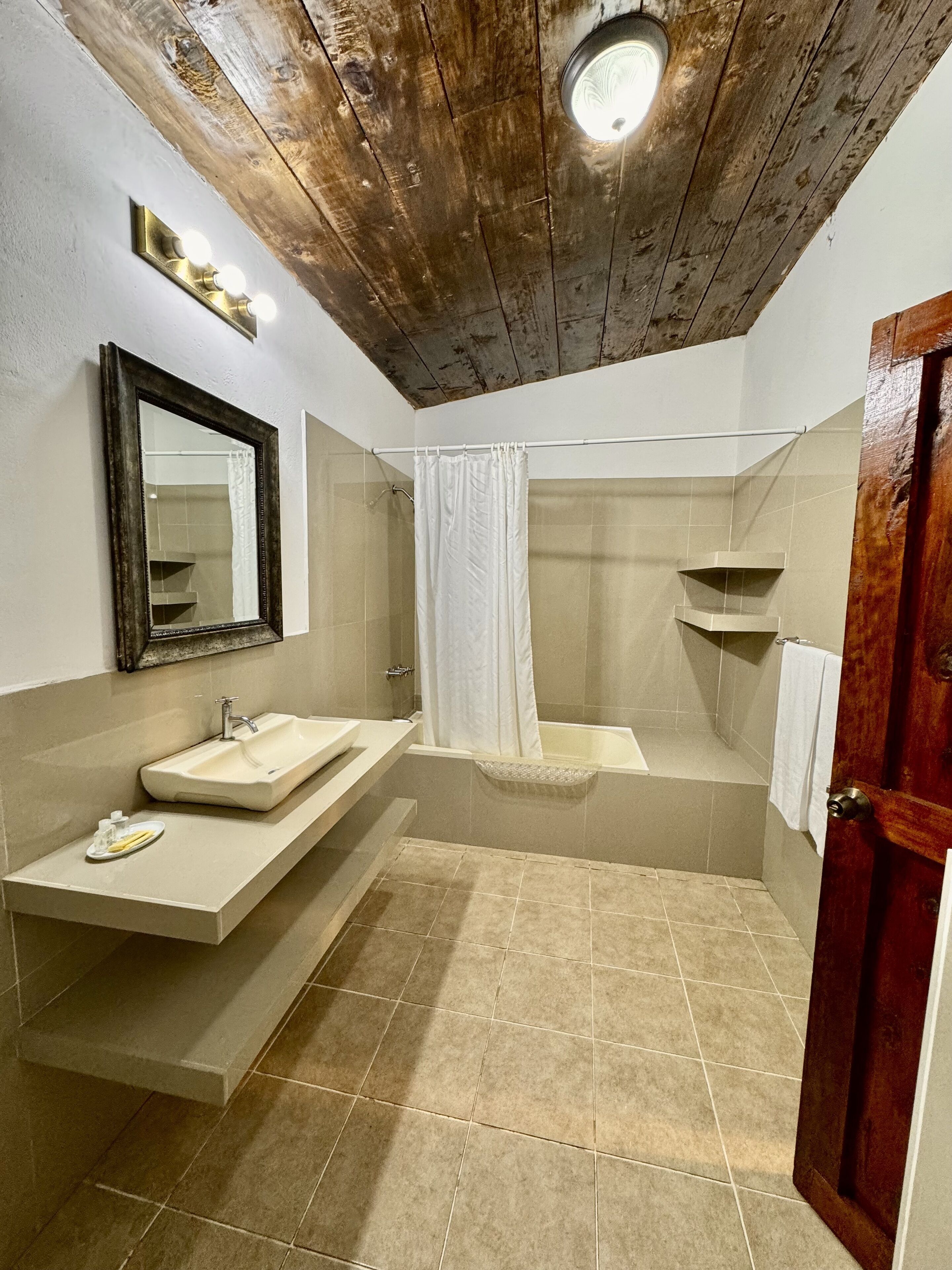 A bathroom with a wooden ceiling, a sink, a bathtub, and a mirror.