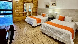 Ein Zimmer in einer Holzhütte mit zwei Betten, einem Deckenventilator und einem Fenster mit Vorhängen.