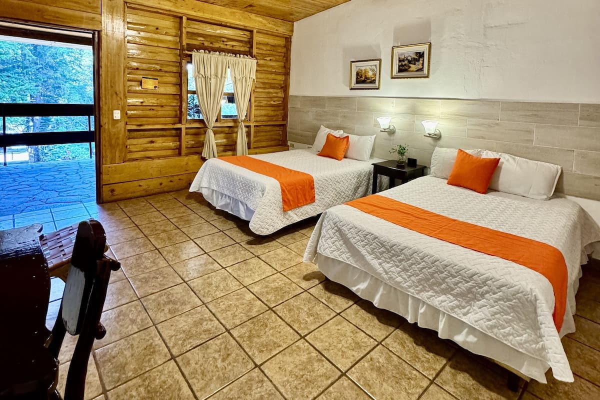 Una habitación tipo cabaña de madera con dos camas, un ventilador de techo y una ventana con cortinas.