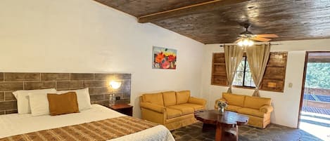 A room with a large bed, two sofas, a coffee table, and a ceiling fan.