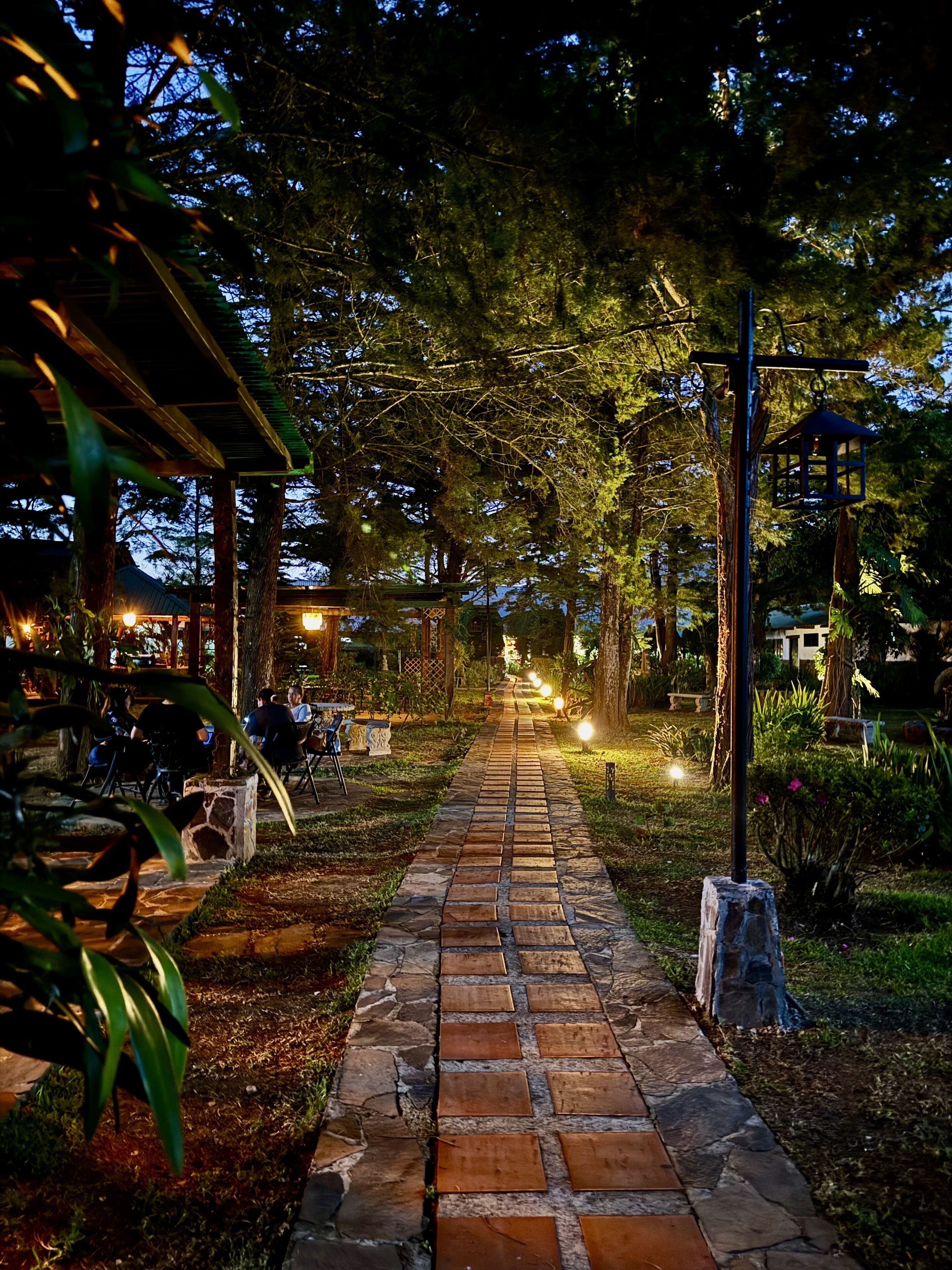 Un chemin de pierres qui traverse un jardin agrémenté d’arbres et d’un kiosque.