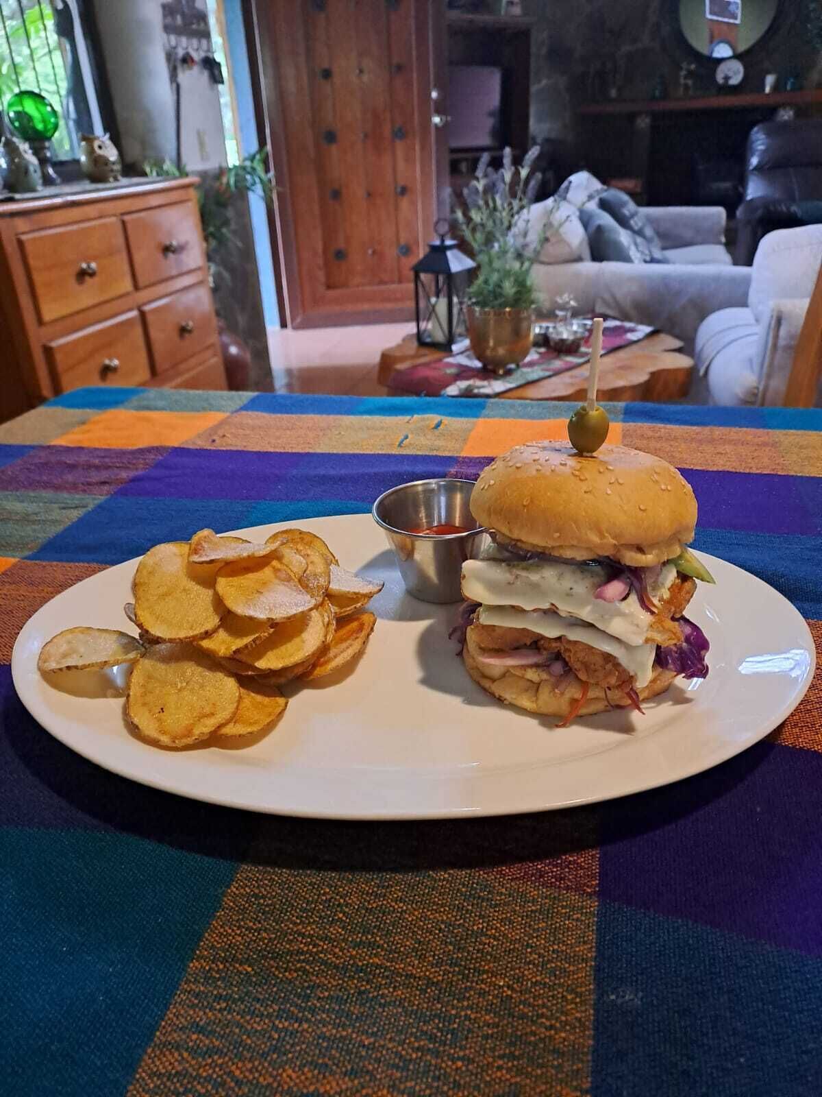 Ein Teller mit einem Sandwich und Kartoffelchips auf einer bunten Tischdecke.