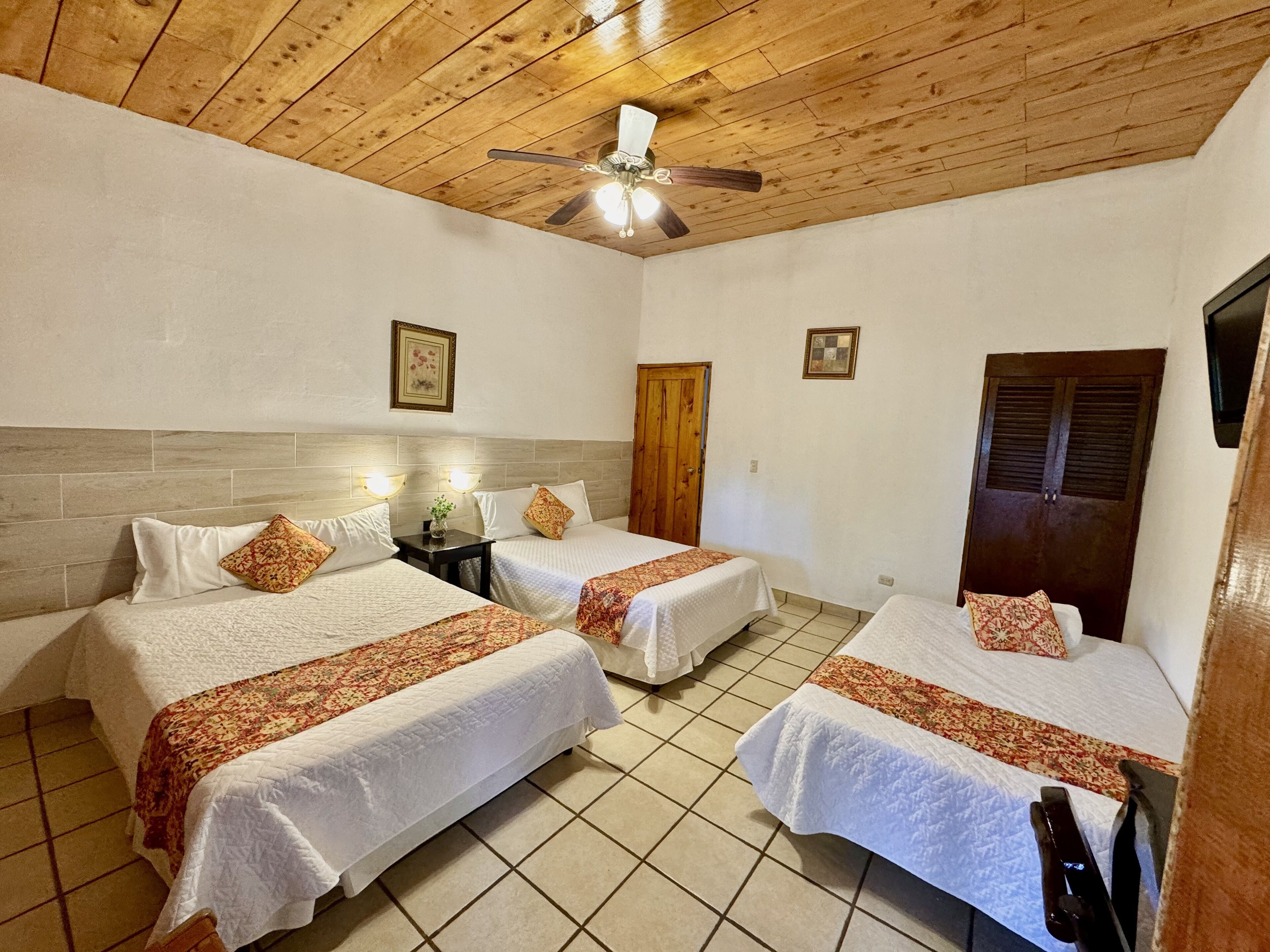 A hotel room with two beds, wooden ceiling, tiled floor, and a ceiling fan.