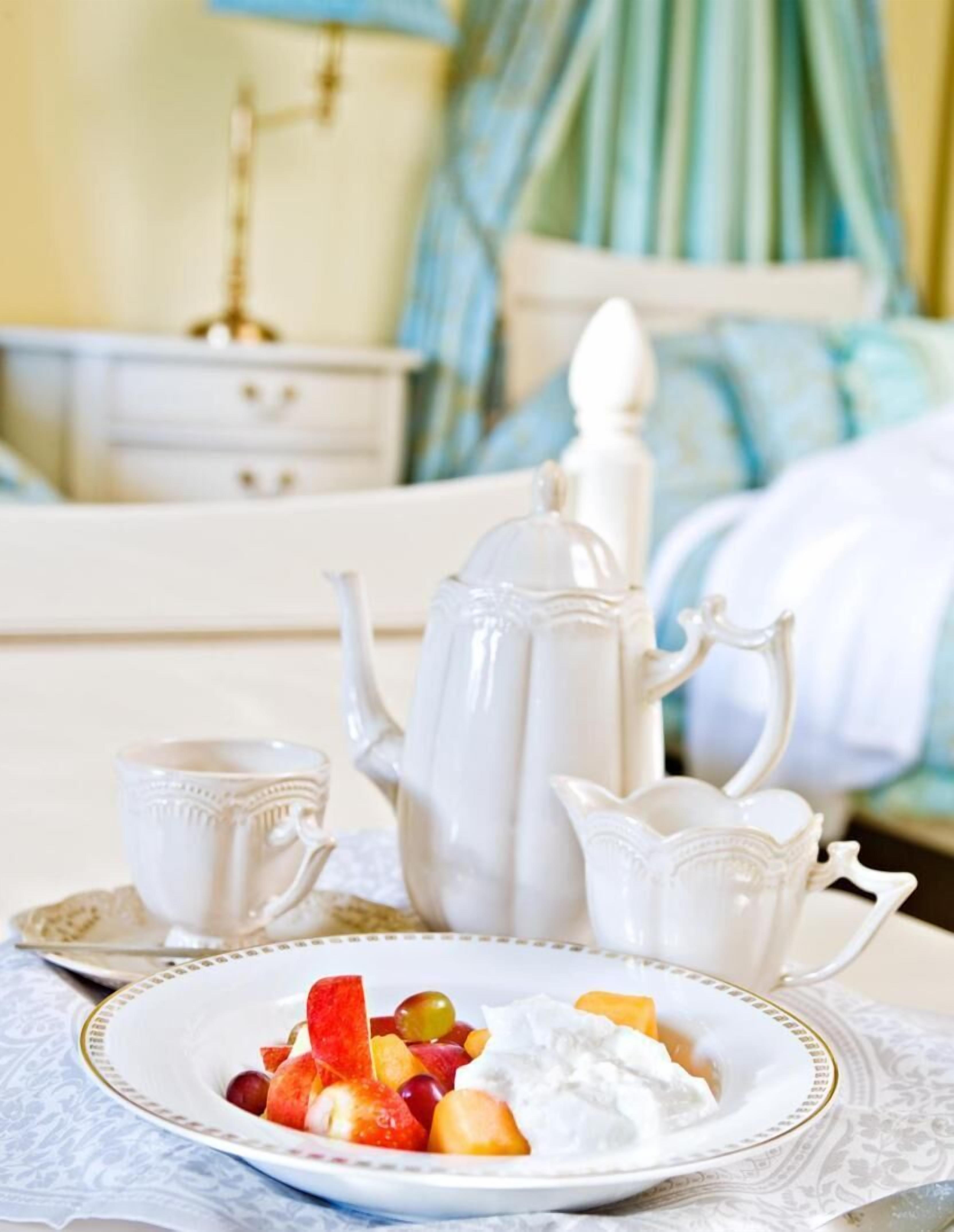 Un desayuno con un plato de fruta y yogur, una tetera y una taza sobre una mesa.