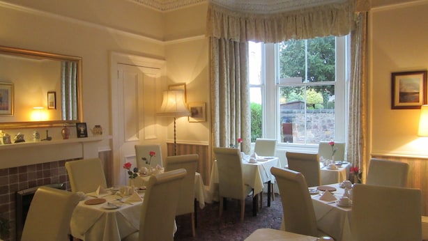 A dining area with multiple tables and chairs, a chandelier, and a large window with curtains. - Sonas Guesthouse (Edinburgh)