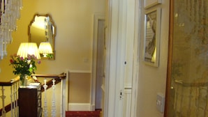 A hallway with a red carpet, a mirror, a lamp, and a framed picture on the wall. - Sonas Guesthouse (Edinburgh)