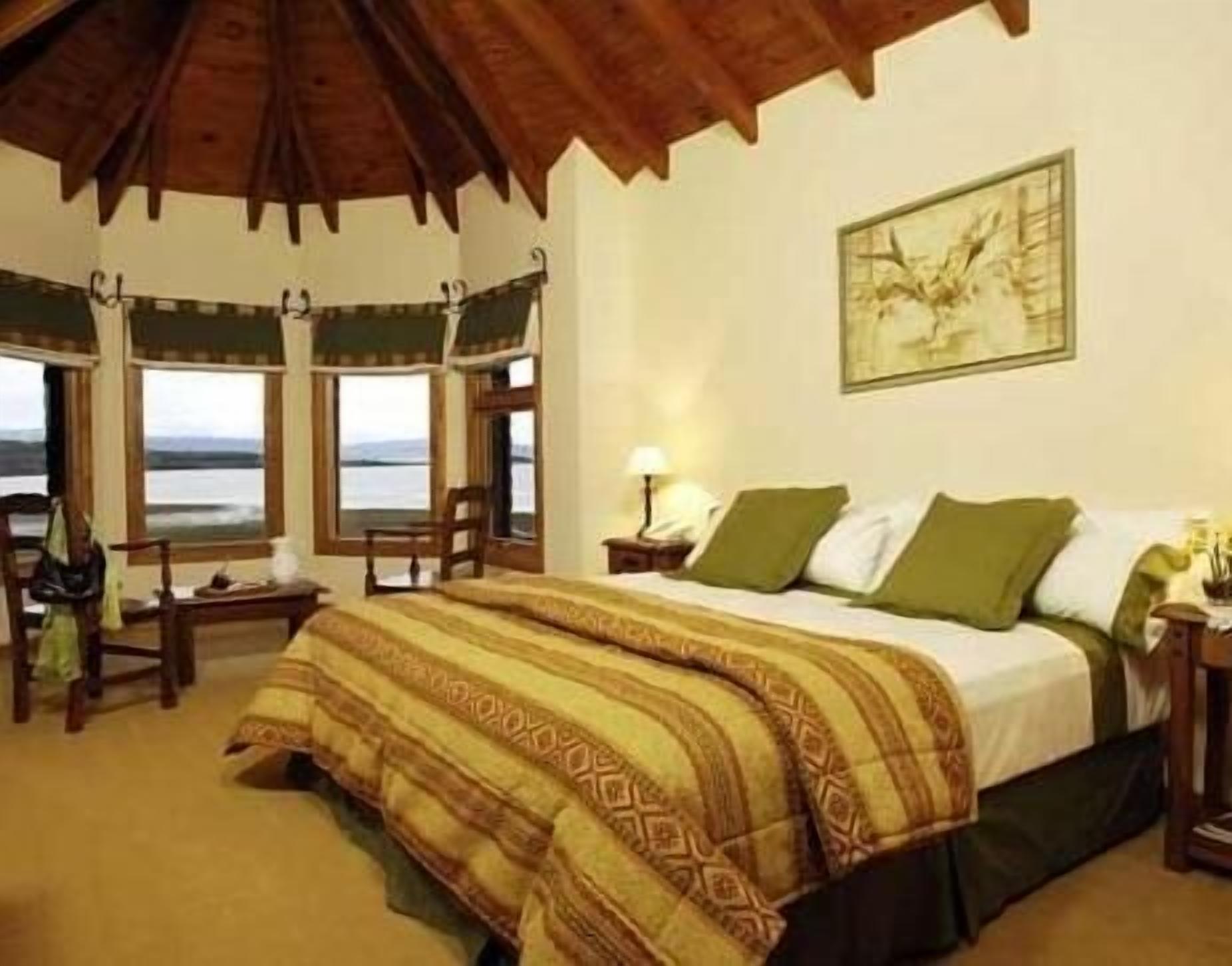 A bedroom with a bed, a chair, a nightstand, a lamp, and a window with a view.