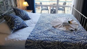 Una cama con edredón y almohadas de diseño azul y blanco, una toalla doblada cuidadosamente y un balcón con sillas y barandilla.