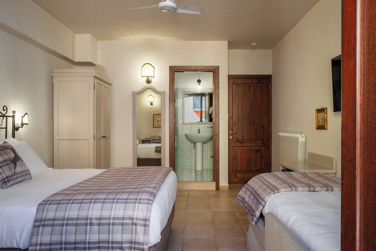 A bedroom with two beds, a bathroom with a sink and mirror, and a ceiling fan.