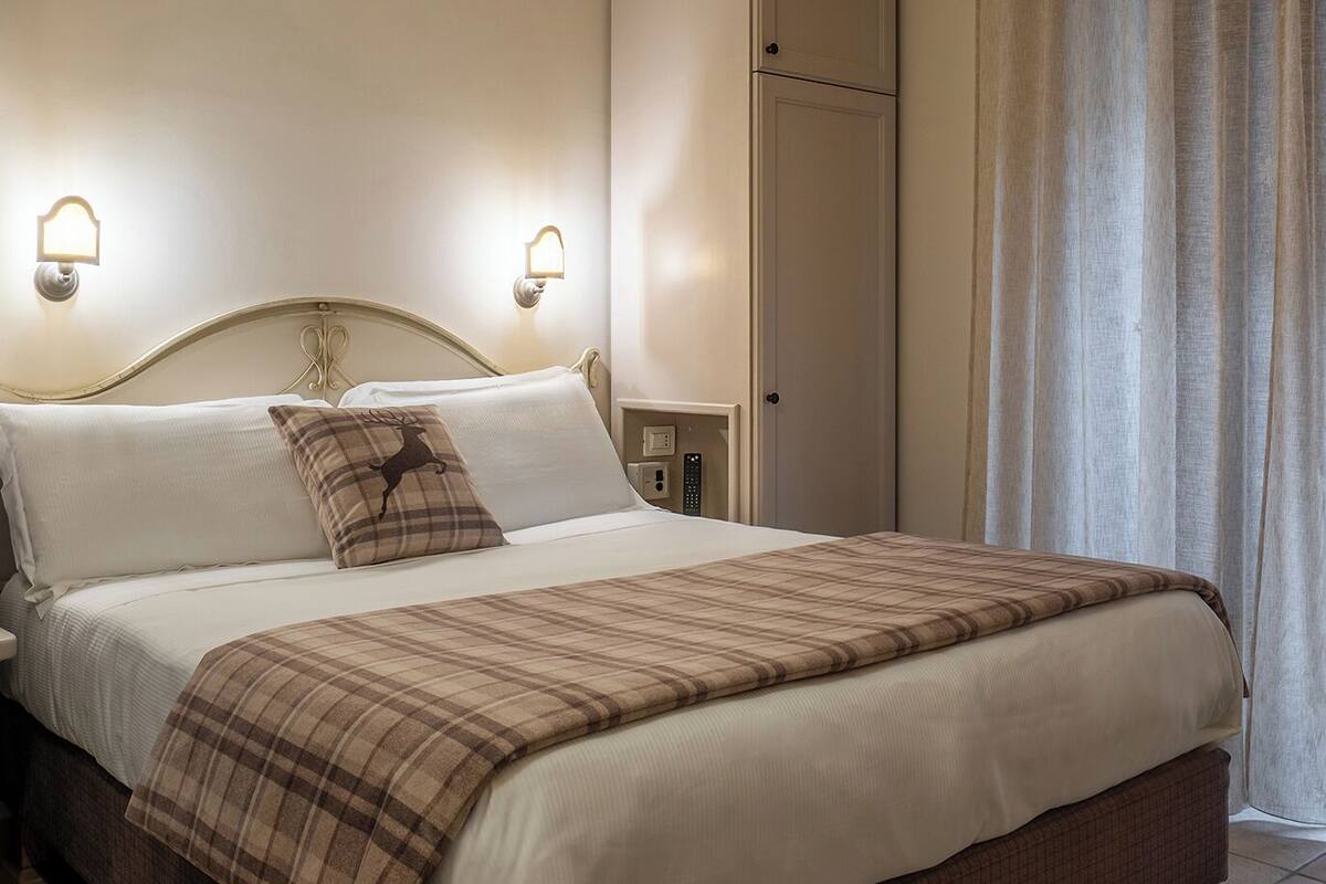 A bedroom with a bed, bedside lamps, a ceiling fan, a wardrobe, and a window with curtains.