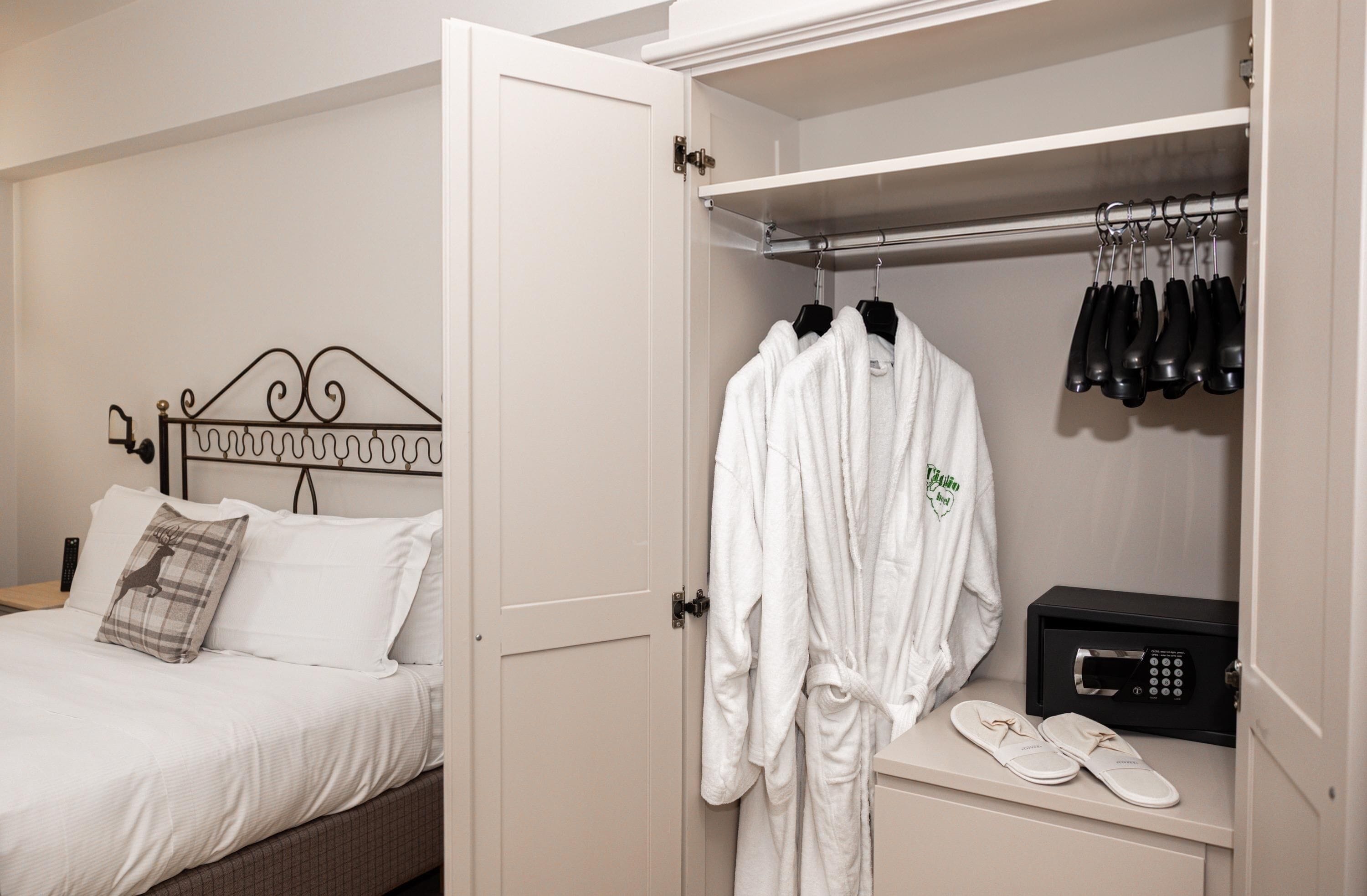 A hotel room with a bed, a robe hanging on a rack, slippers, and a radio.