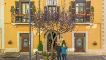 A yellow building with a tree in front, two doors, and a bench.