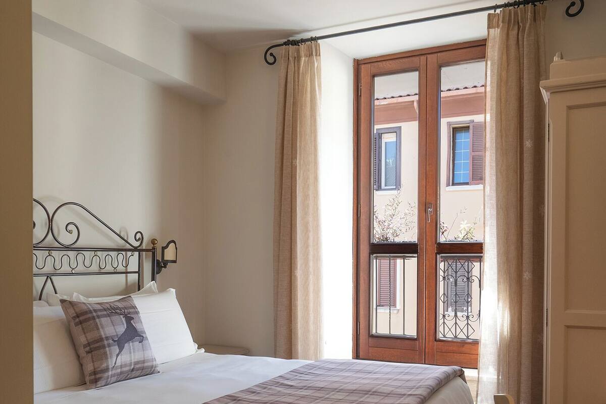 A bedroom with a bed, a ceiling fan, a window with curtains, and a view of the outside.