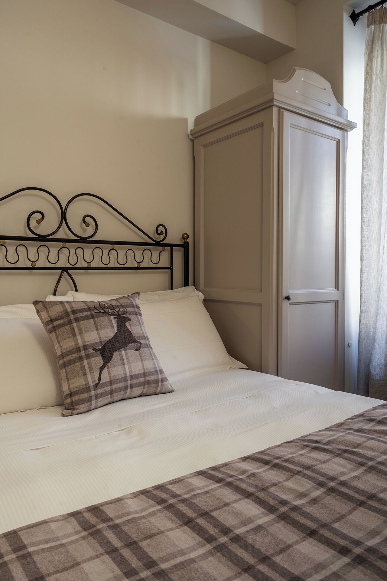 Una cama con una manta escocesa, un almohadón con diseño de ciervo y un cabecero de metal.
