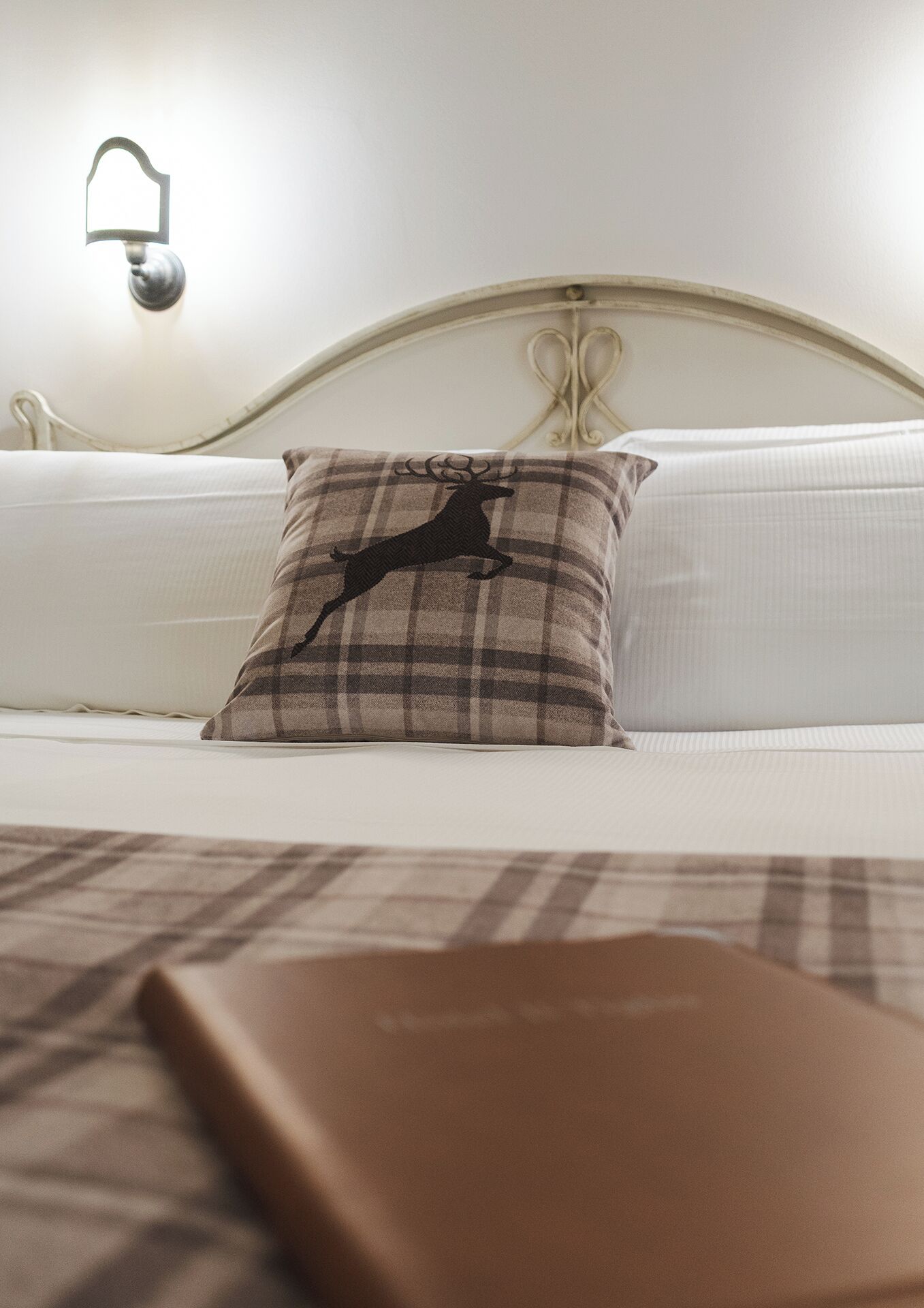 Una cama con un almohadón escocés y un libro marrón encima.