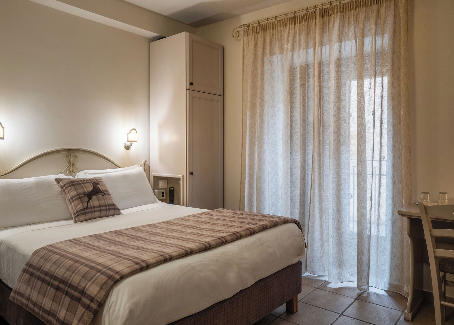 Un lit bien fait, recouvert d’une couverture à carreaux, une table de chevet avec une lampe et une armoire.