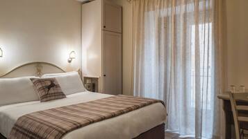 Ein ordentlich bezogenes Bett mit einer Karo-Decke, ein Nachttisch mit Lampe und ein Kleiderschrank.
