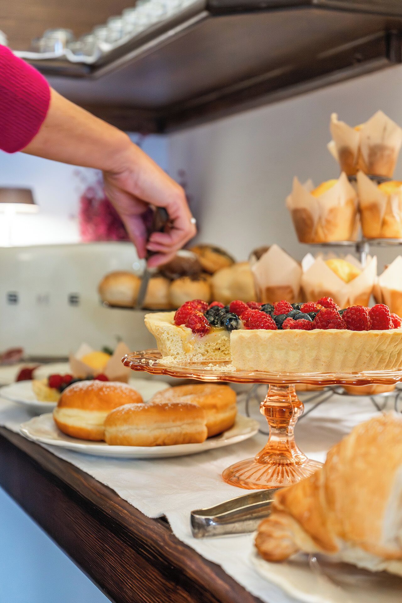 A buffet with various pastries and a person serving food.