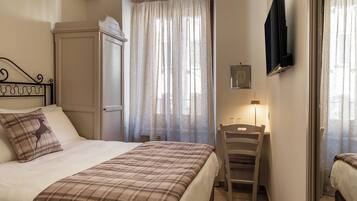 Un dormitorio con cama, una silla, un escritorio, un televisor y una ventana con cortinas.