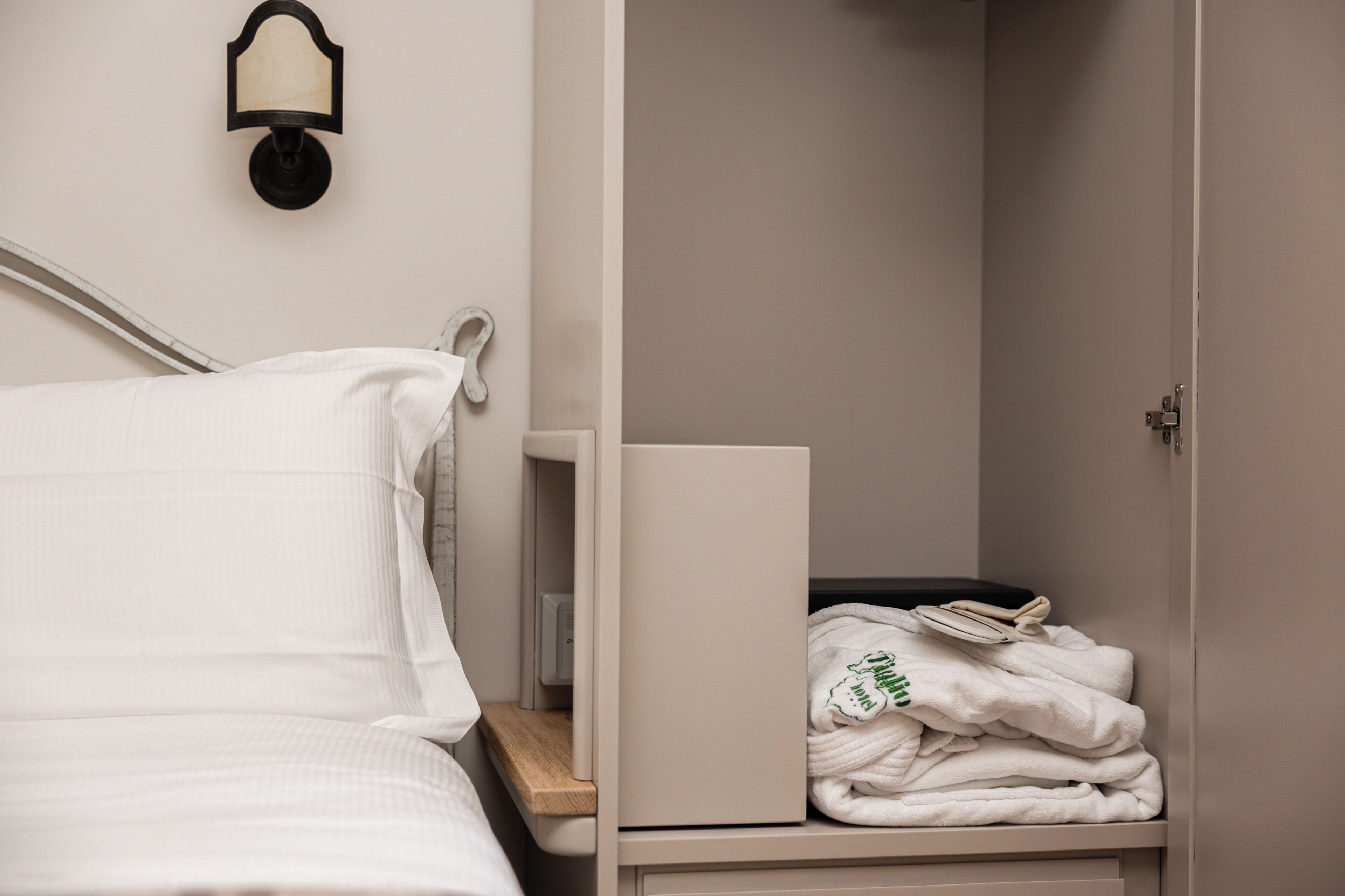 Habitación de hotel con una cama, una mesita de noche, una lámpara de pared y un armario con toallas dobladas.