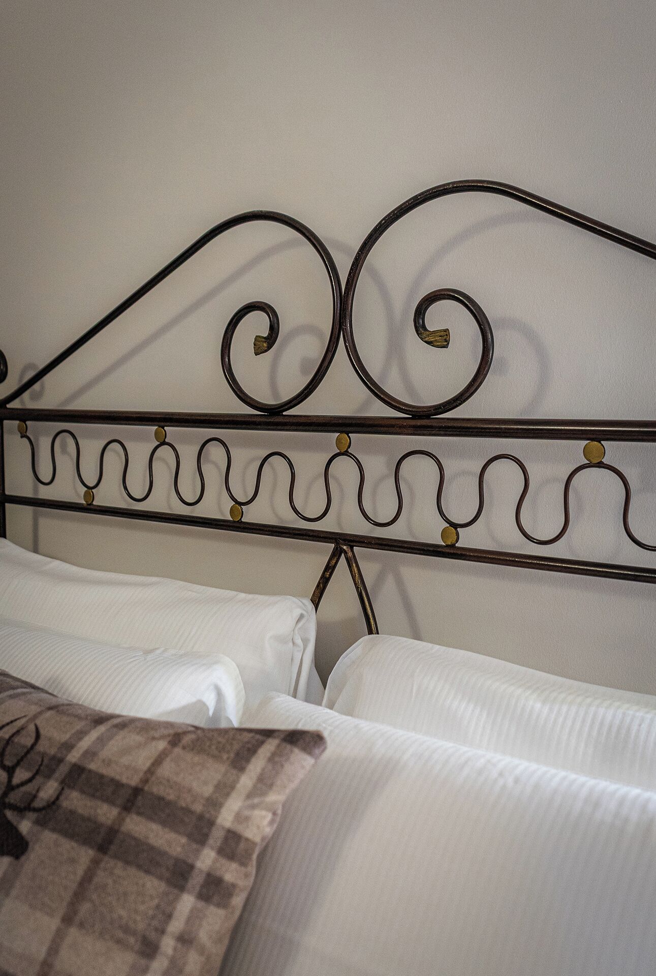 Una cama con sábanas blancas y cabecera de metal con adornos en espiral.