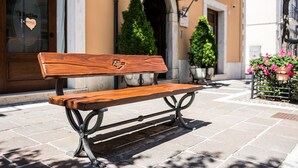 A wooden bench with a heart-shaped emblem, located on a paved sidewalk in front of a building with a glass door and a sign that reads "Hotel." - Hotel Il Tiglio (Castel di Sangro)