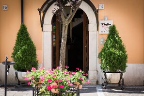 Entrada de hotel con un letrero que dice "Tiglio hotel", dos árboles en macetas y un arreglo floral.