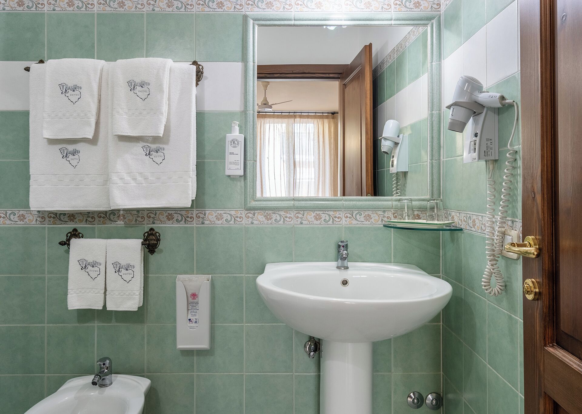 A bathroom with green tiles, a white sink, a mirror, and towels with a heart design.