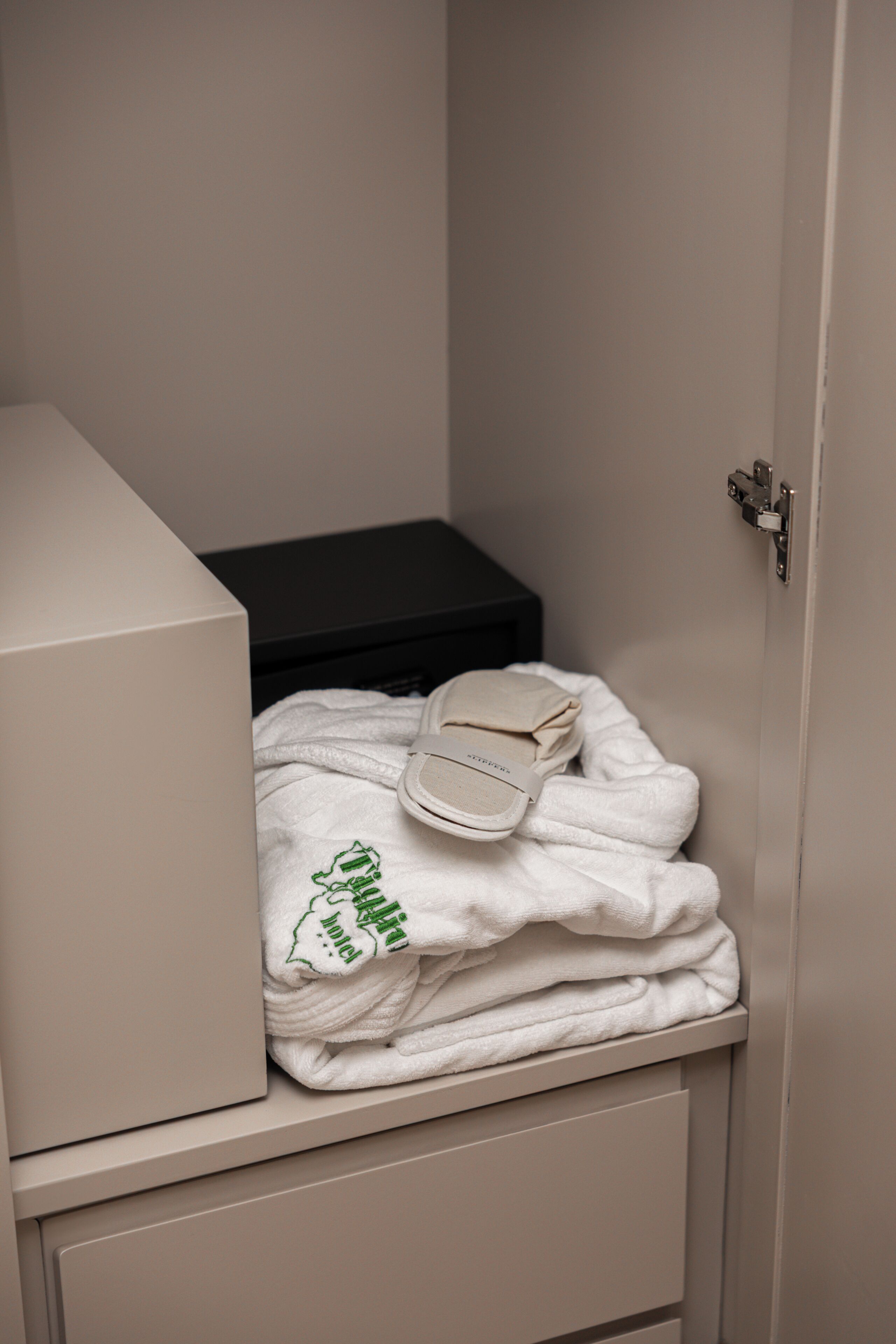 A bathroom with a towel stack, a white robe, and a pair of slippers on a shelf.