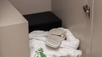 A bathroom with a towel stack, a white robe, and a pair of slippers on a shelf.