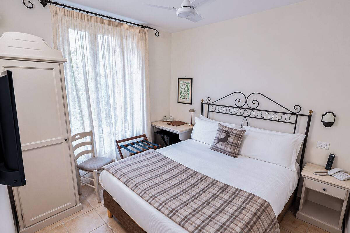 A bedroom with a bed, a desk, a chair, a wardrobe, and a nightstand with a phone.