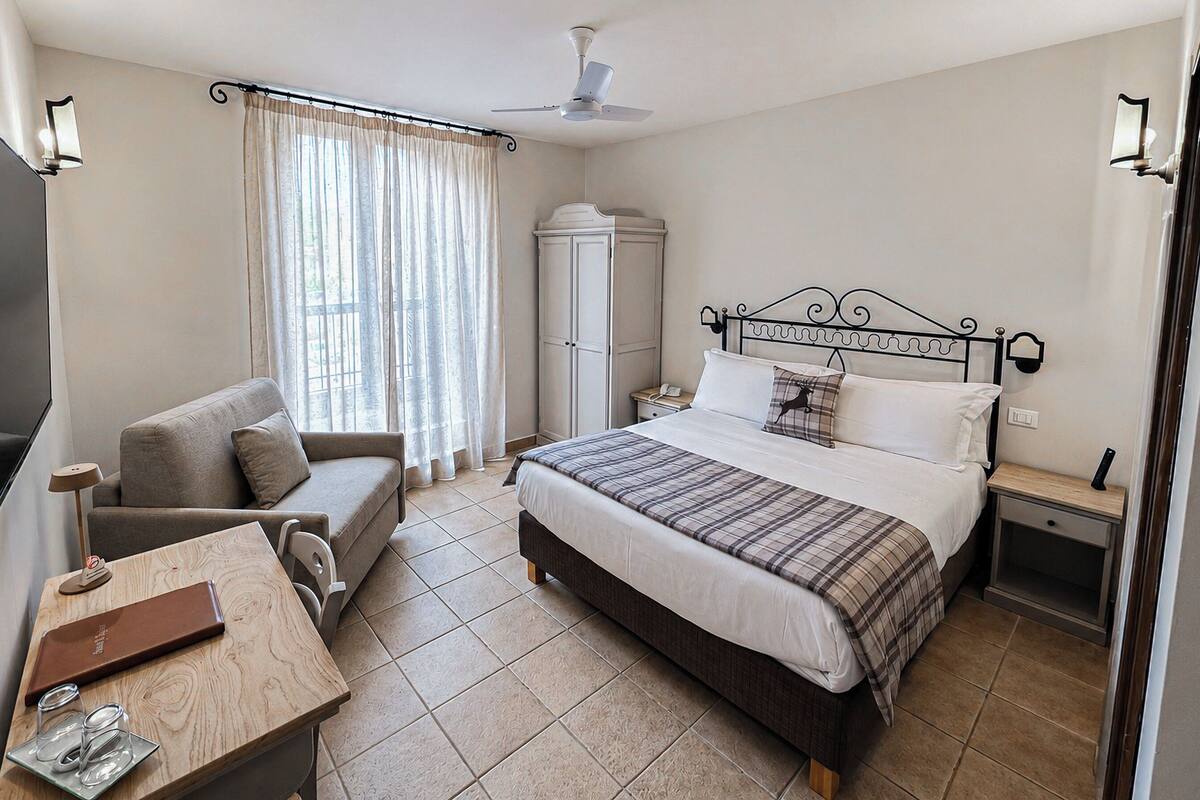 A hotel room with a bed, a desk, a chair, a wardrobe, and a ceiling fan.